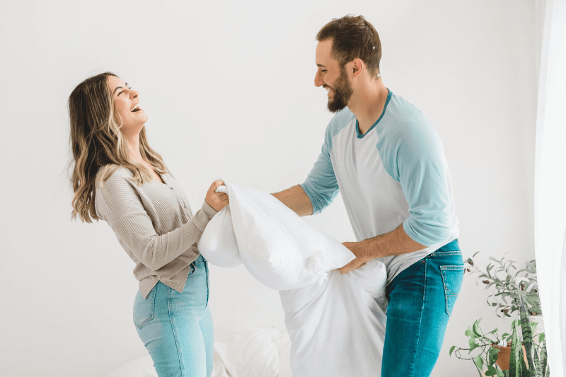 A cheerful young couple enjoying a playful moment in their new home, holding a pillow and laughing. The bright and inviting interior, filled with natural light, reflects a comfortable living environment. This image represents the successful placement of qualified tenants, a service provided by Carolina Property Management Company to help landlords maintain happy and reliable renters in their properties.