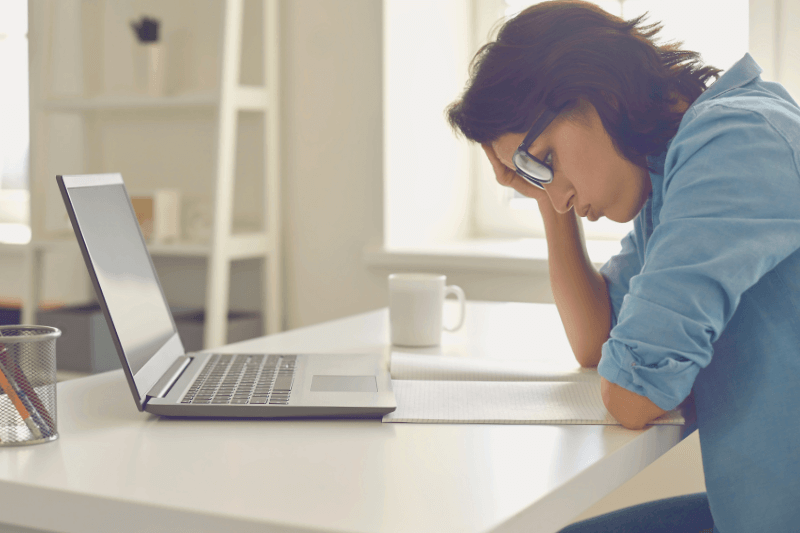 A stressed landlord sitting at a desk with a laptop and paperwork, resting her head on her hand. The scene depicts the challenges landlords face when screening tenants on their own. Carolina Property Management LLC offers professional tenant screening services to alleviate this burden and ensure landlords find qualified and reliable tenants for their properties.