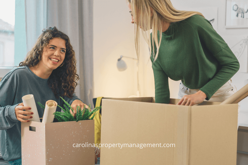 Two young women happily unpacking boxes in their first apartment, sharing a moment of excitement as they organize their new space. This scene reflects the beginning of a rental experience, supported by Carolinas Property Management Company, ensuring a seamless transition and offering guidance for first-time renters.