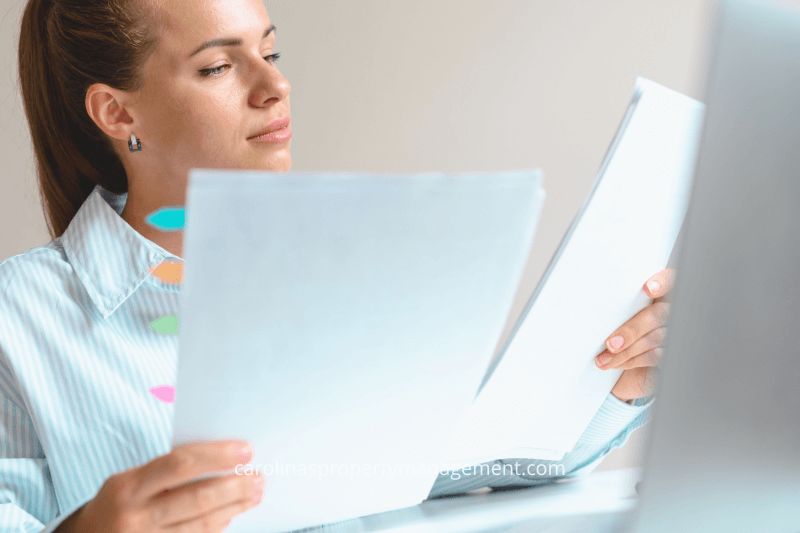 A professional woman reviewing tenant application documents at her desk with a laptop. This image illustrates how Carolina Property Management Company ensures thorough tenant screening and document verification, providing a better experience than Zillow’s application process.